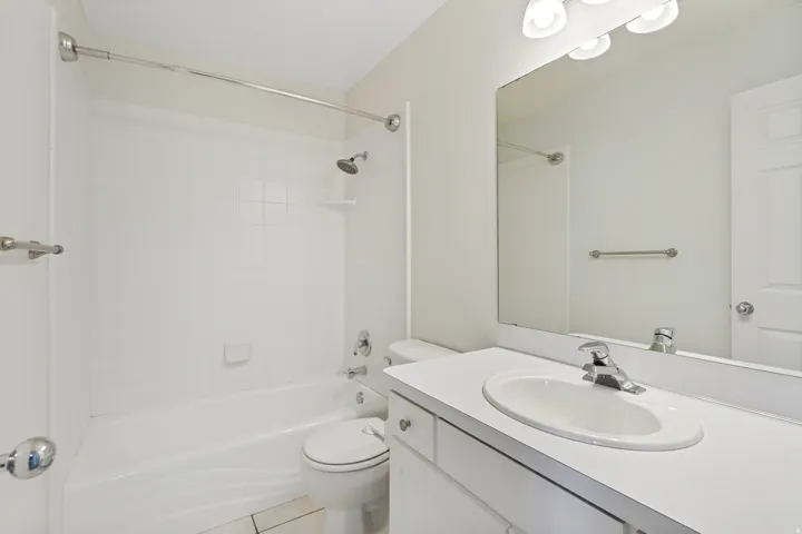 Bathroom featuring a white bathtub, shower with a chrome showerhead, white tiled walls, a vanity with an integrated sink, and a large wall-mounted mirror