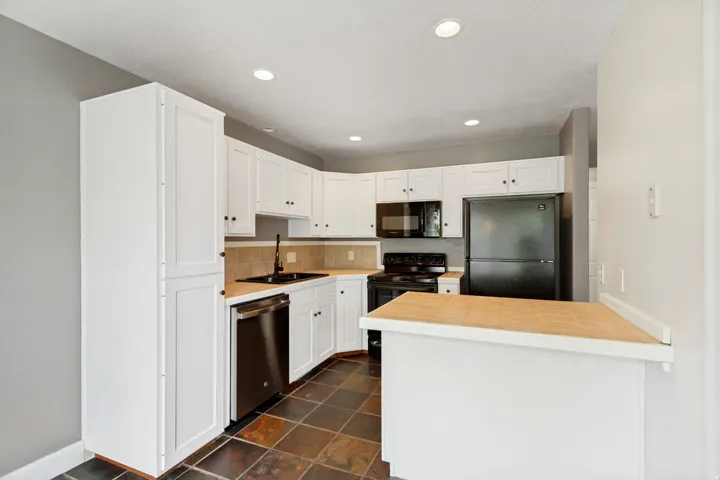 White cabinetry, stainless steel dishwasher, black appliances, tile backsplash, and recessed lighting