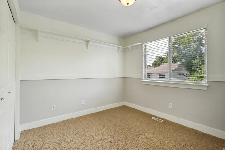Built-in closet shelving, carpeted flooring, and a large window with blinds