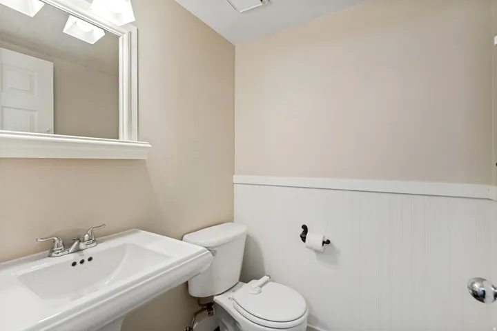 Pedestal sink with chrome faucet, framed mirror, vanity lighting, and wainscoting