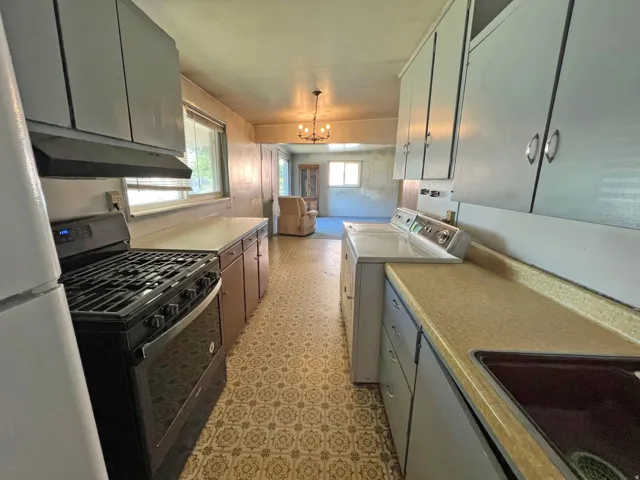 Galley kitchen featuring a gas range, white cabinetry, integrated sink, and an adjacent laundry area with a washing machine and dryer