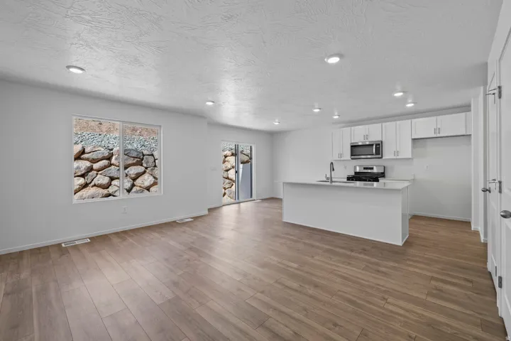 Open-concept living space with wood-finish flooring, recessed lighting, and a kitchen featuring white cabinetry, stainless steel appliances, and an island with an integrated sink