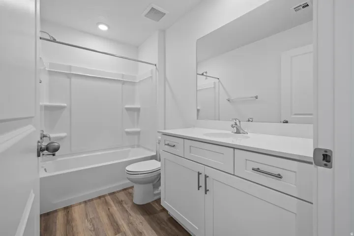 Wood-finish flooring, white vanity with ample storage, integrated sink, bright white countertop, and expansive mirror