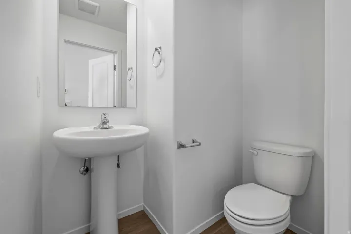 Pedestal sink with chrome faucet, wall-mounted mirror, and wood-finish flooring