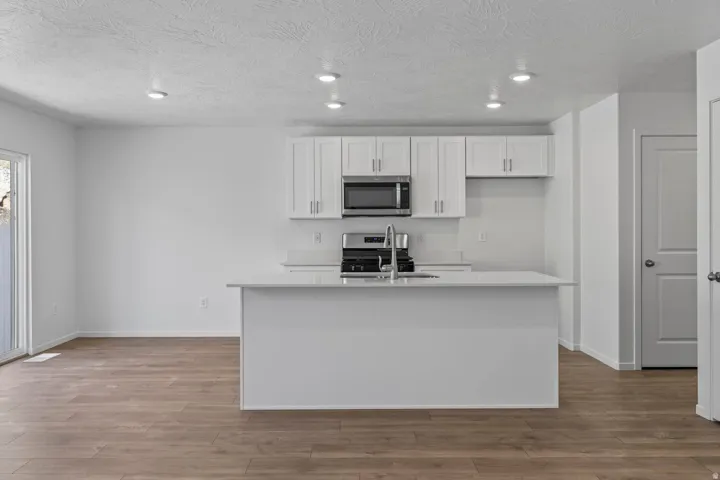 Kitchen featuring white cabinetry, stainless steel appliances, a center island with sink, and wood-finish flooring