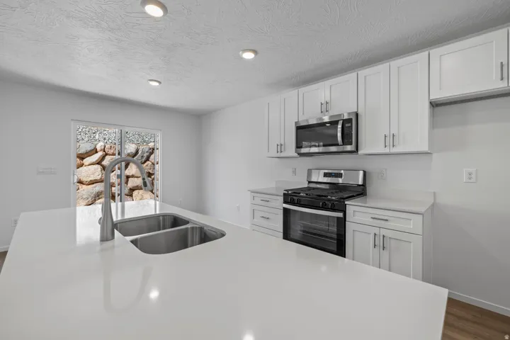 Kitchen featuring white cabinetry, stainless steel appliances, a double basin sink, light-toned countertops, and recessed lighting