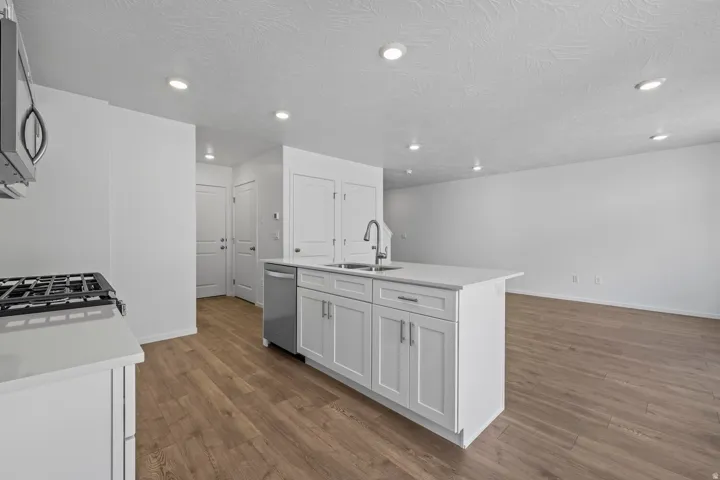 Kitchen island featuring white shaker cabinetry, an undermount sink, and stainless steel appliances including a gas range and dishwasher