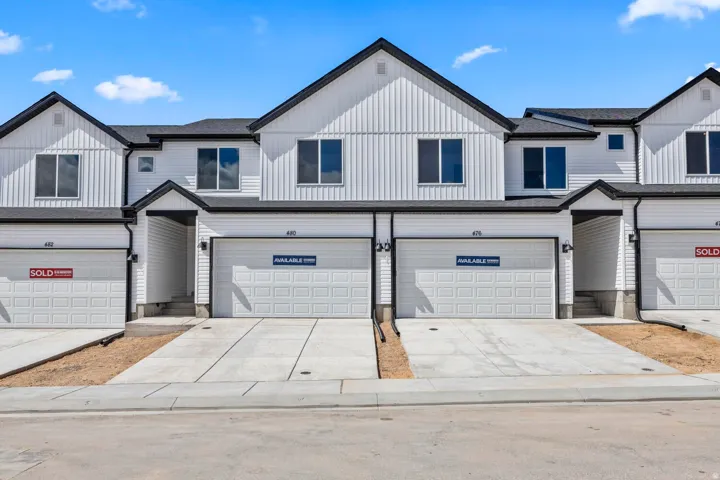 Townhome exterior featuring white vertical and horizontal siding, dark trim, an attached garage, and a concrete driveway