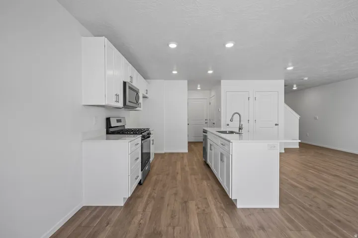 Kitchen featuring white cabinetry, stainless steel appliances, an island with an integrated sink, and wood-finish flooring