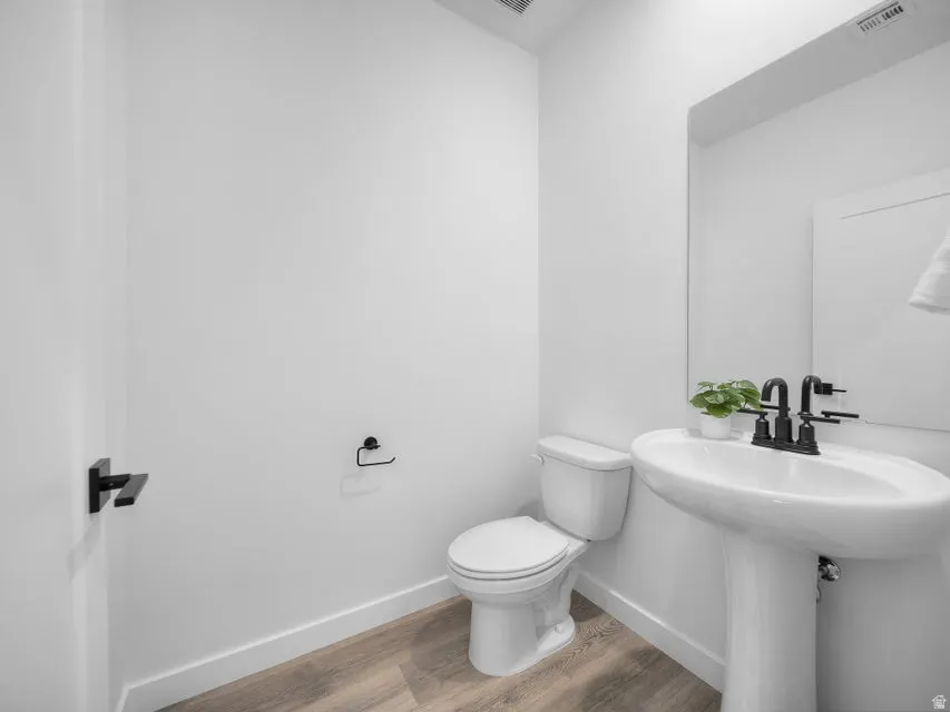 Pedestal sink with matte black hardware, wood-finish flooring, and a wall-mounted mirror