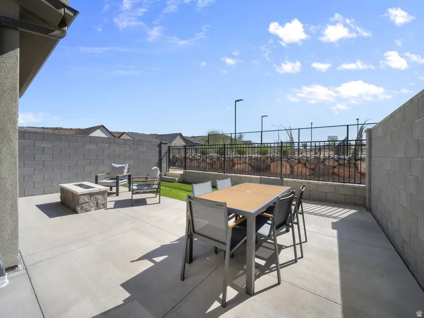 Expansive concrete patio with a built-in fire pit, artificial turf landscaping, and perimeter block wall fencing