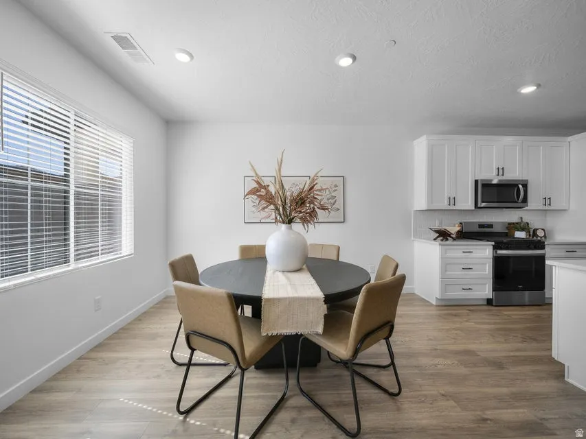 Wood-finish flooring, recessed lighting, white kitchen cabinetry, stainless steel appliances, and a window with blinds