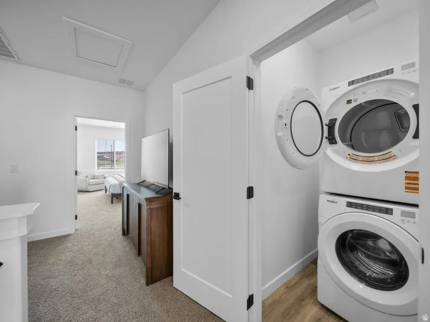 Dedicated laundry area with stacked appliances, wood-finish flooring, and white paneled doors with dark hardware