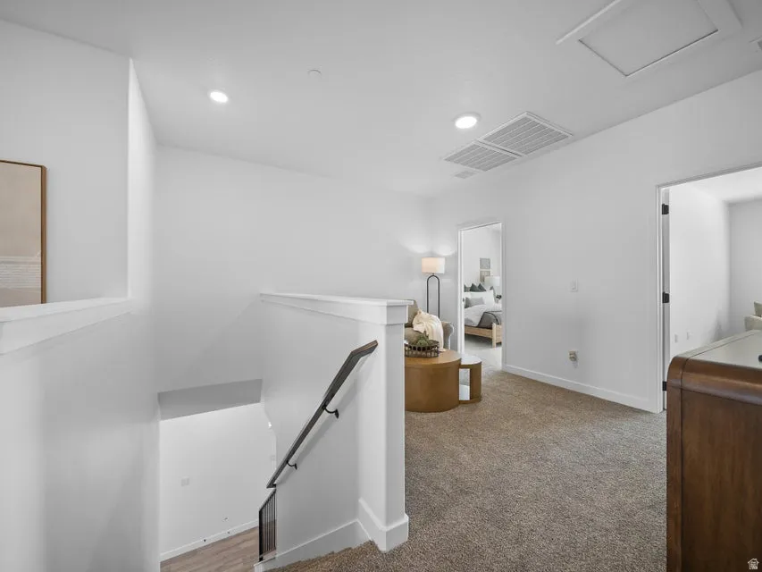 Carpeted upper-level landing with recessed lighting, white walls, and a modern dark-finish handrail