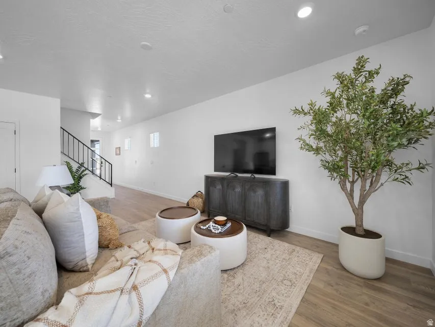 Recessed lighting, wood-finish flooring, white walls, and a black wrought iron staircase railing