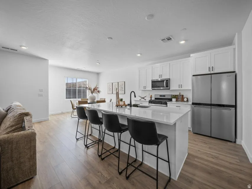 Contemporary kitchen island with a white countertop, white cabinetry, stainless steel appliances, and wood-finish flooring