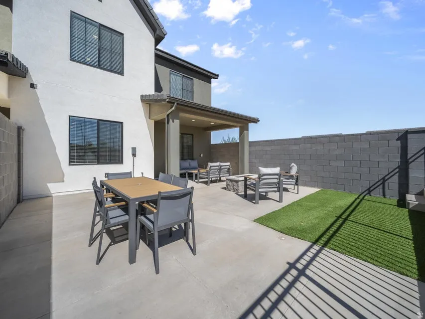 Expansive concrete patio with dedicated artificial turf area, privacy block wall, and covered patio structure