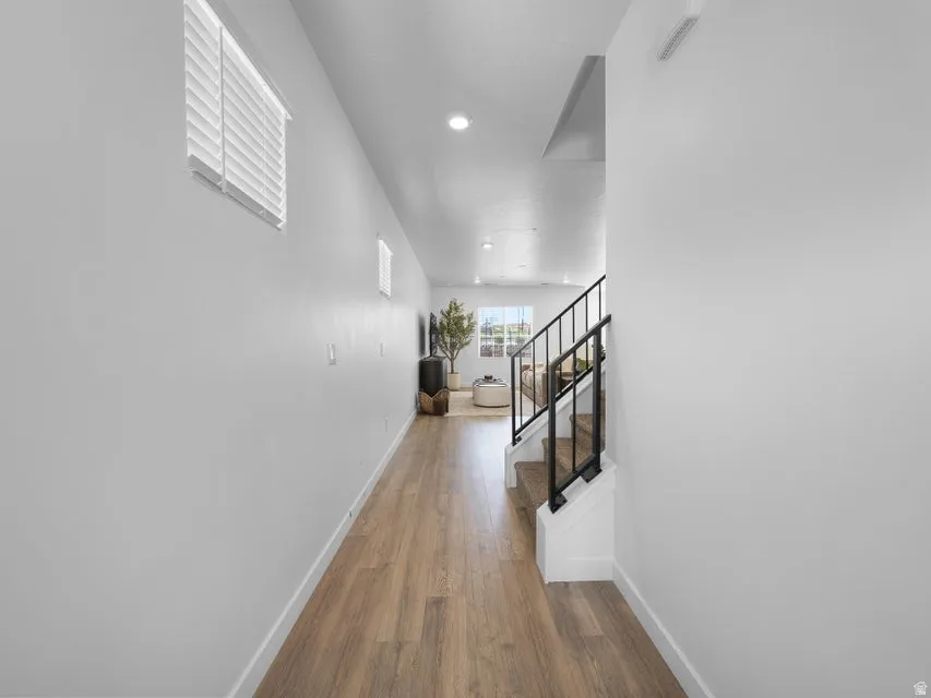 Wood-finish flooring with recessed lighting, white walls, and a staircase featuring black metal railings