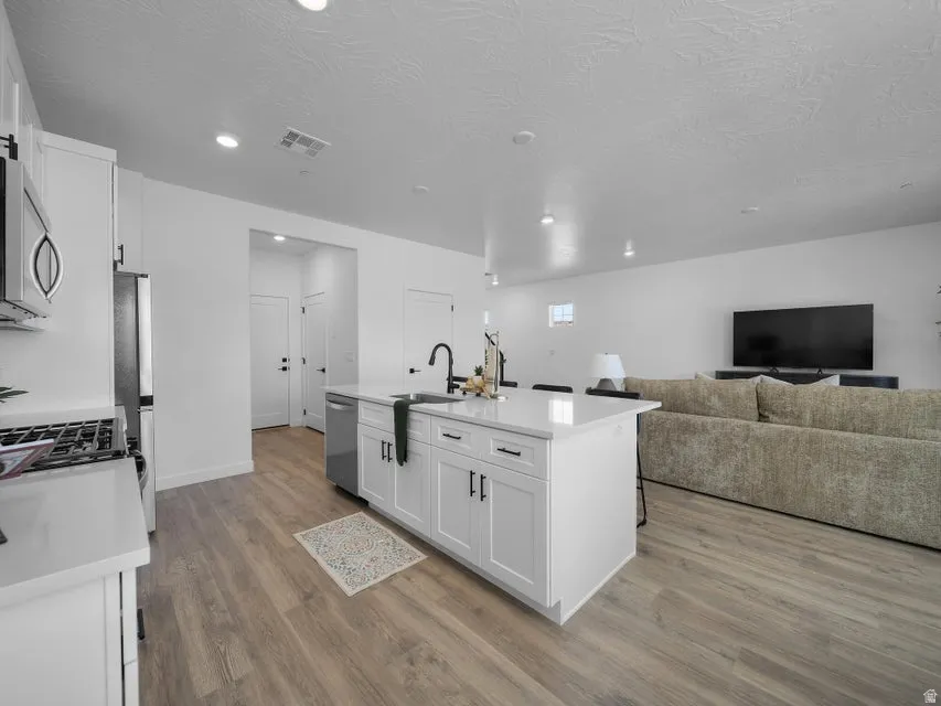 White cabinetry with black hardware, stainless steel appliances, and a central island with an integrated sink