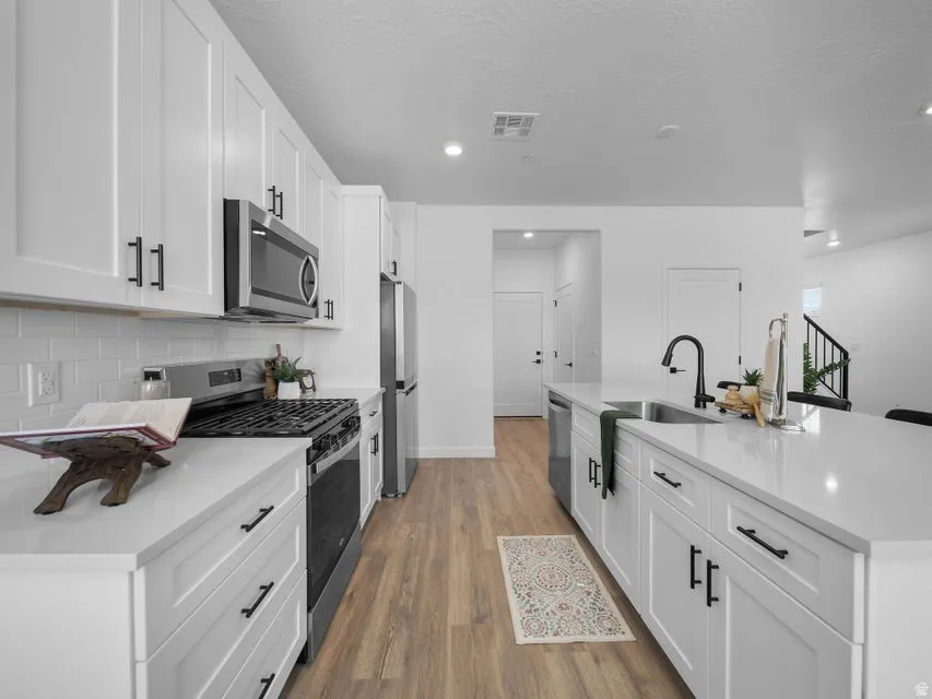 Kitchen featuring white shaker-style cabinetry, stainless steel appliances, a subway tile backsplash, light-toned countertops, and wood-finish flooring