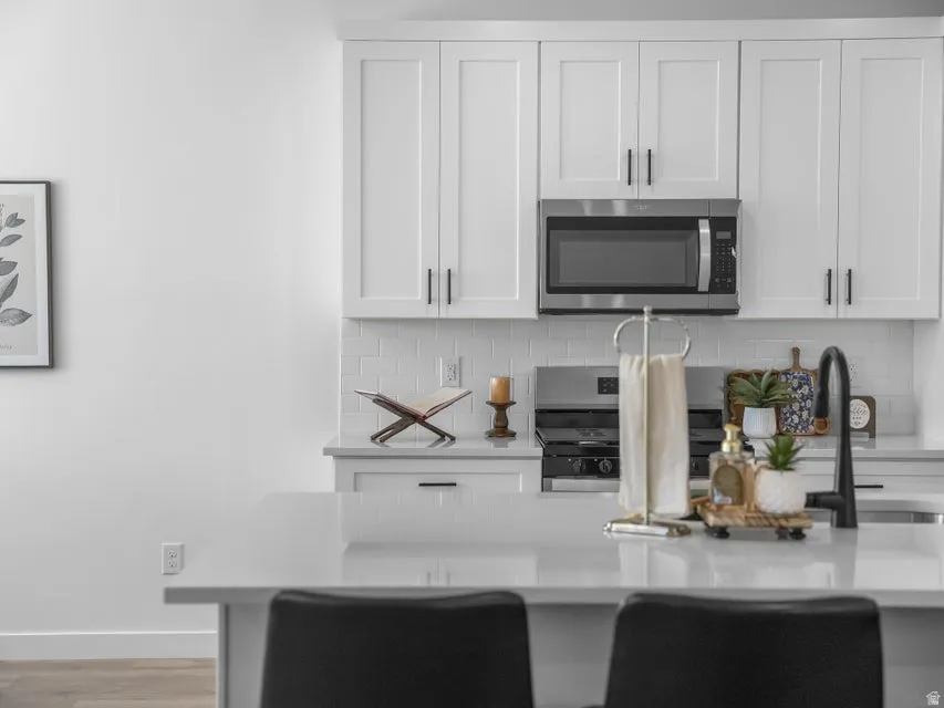 White shaker cabinetry, stainless steel microwave, subway tile backsplash, and a black gooseneck faucet