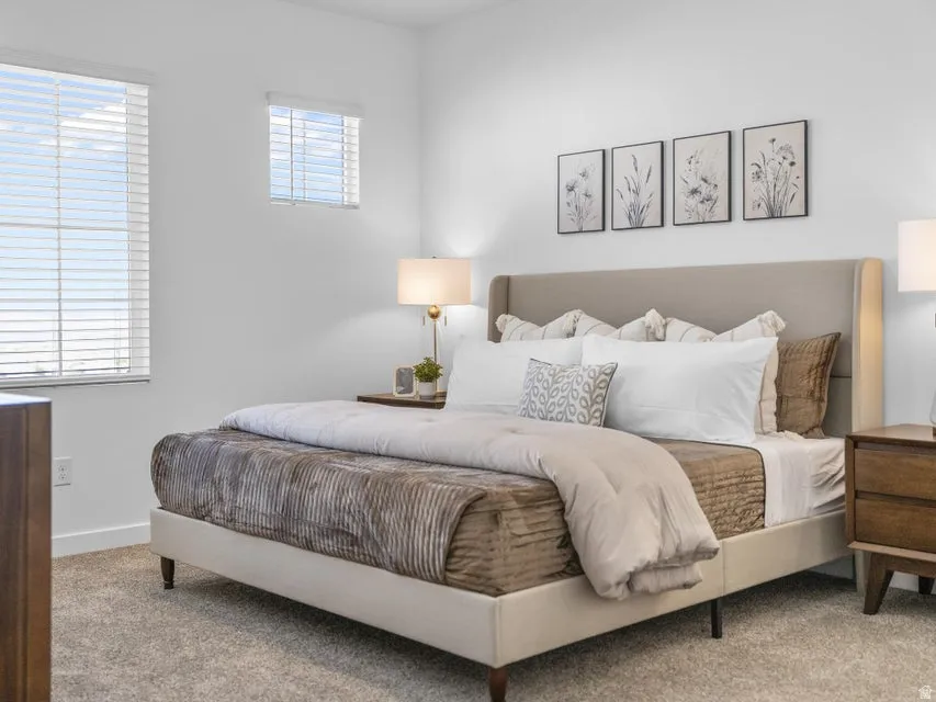 Carpeted flooring, white walls, two windows with blinds, and a built-in upholstered headboard