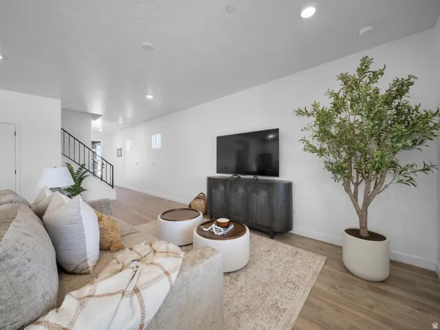 Recessed lighting, wood-finish flooring, white walls, and a black wrought iron staircase railing