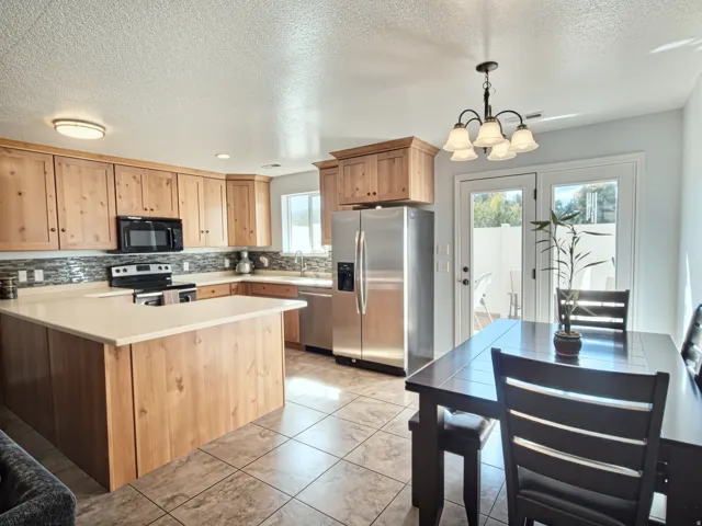 Kitchen featuring natural wood cabinetry, light-toned countertops, stainless steel appliances, and a tiled backsplash