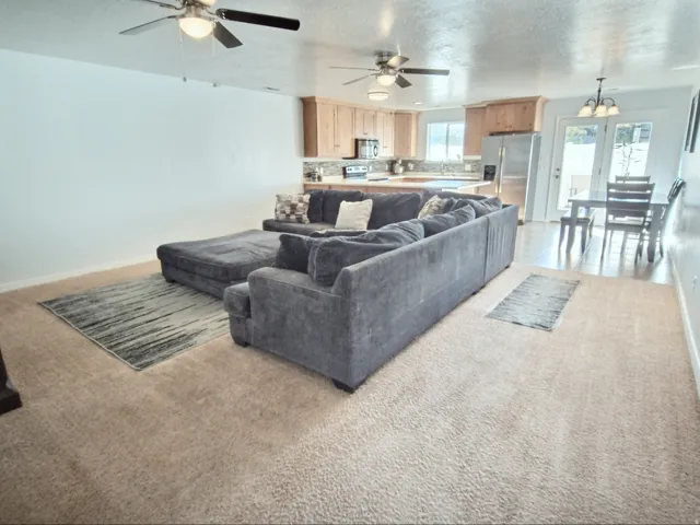 Open-concept living space with ceiling fans, wood-finish cabinetry, stainless steel appliances, and a dining area with pendant lighting and exterior access