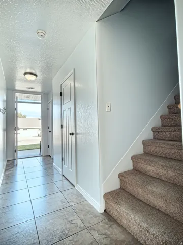 Entryway featuring square tile flooring, a carpeted staircase, and white paneled doors