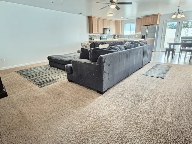 Open concept living area with carpet flooring, light wood-finish cabinetry, stainless steel appliances, and a ceiling fan