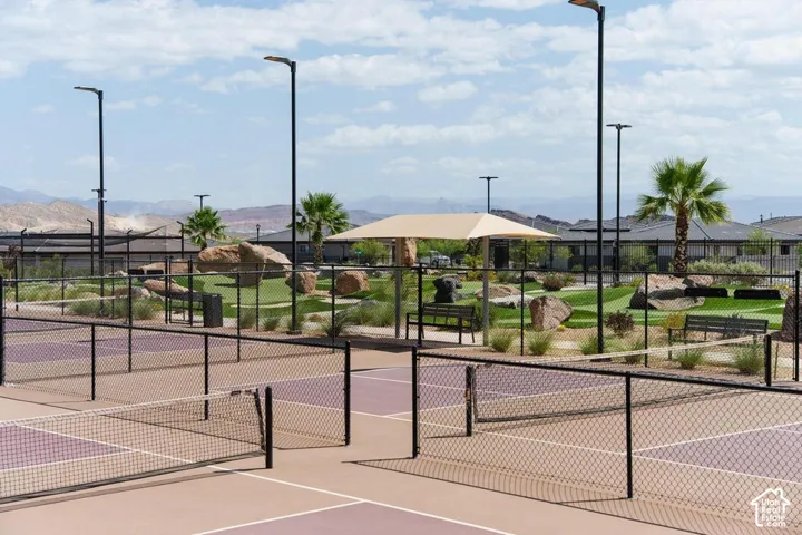 Pickleball courts with black chain-link fencing, surrounded by a landscaped area featuring artificial turf, mature palm trees, and mountain scenery