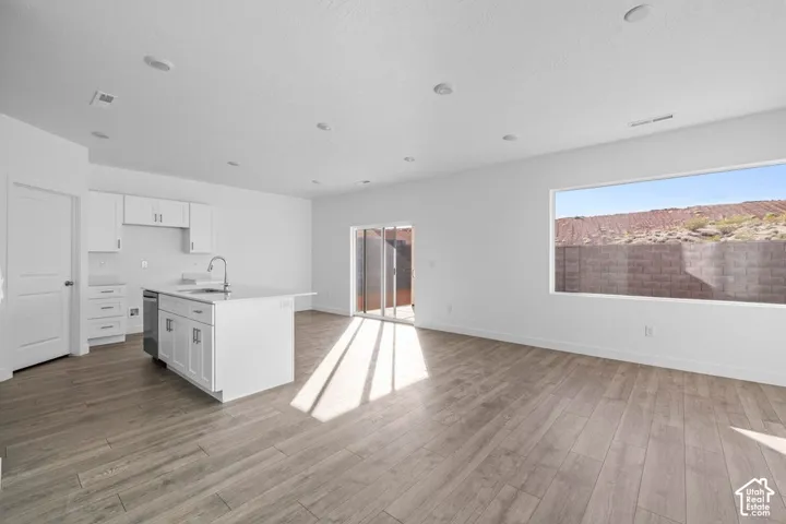 Open-concept living space with wood-finish flooring, white cabinetry, a kitchen island with a stainless steel sink, and a large horizontal window
