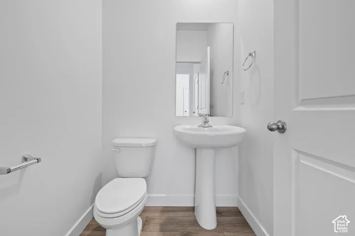 Pedestal sink with chrome faucet, wall-mounted mirror, white toilet, and wood-finish flooring