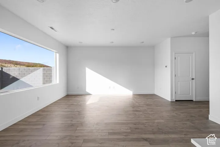 Spacious room with wood-finish flooring, recessed lighting, a large horizontal window, and a paneled interior door with dark hardware