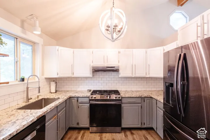Vaulted ceiling kitchen featuring two-tone cabinetry, subway tile backsplash, stainless steel appliances, and a central chandelier