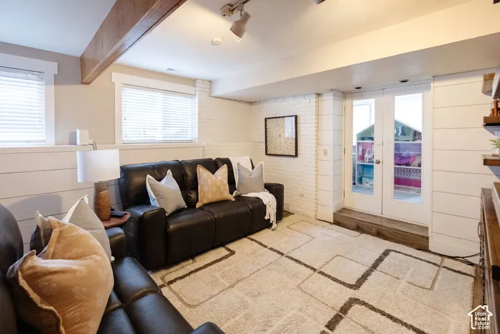 Recessed lighting, exposed wood beam, white painted brick accent wall, white shiplap wainscoting, and white French doors