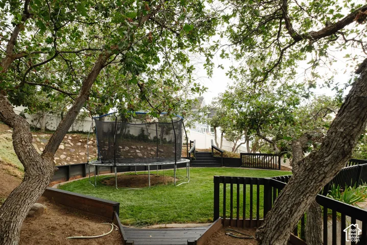 Tiered backyard featuring a manicured lawn, established trees, and dark-stained wood railings