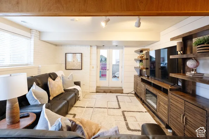 Exposed wood ceiling beam, white painted brick wall, wood-finish built-in shelving, track lighting, and double French doors