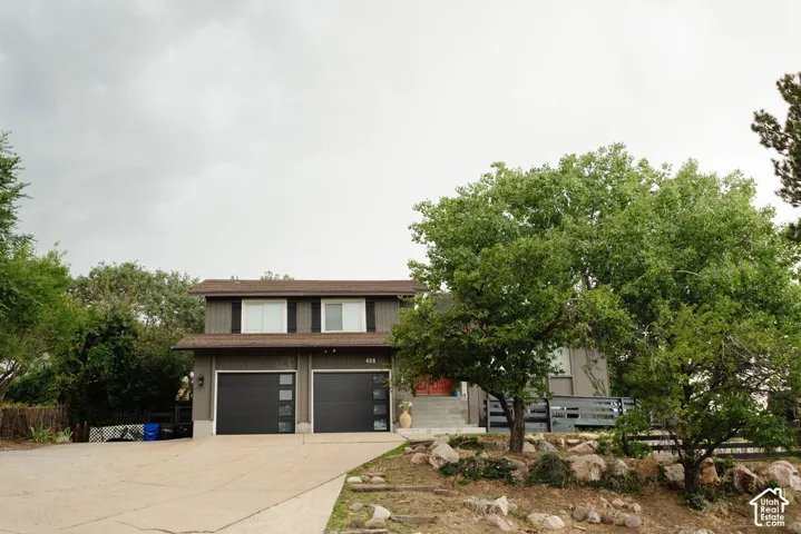 Two-story exterior with dark horizontal siding, dual garage doors featuring frosted glass panels, mature trees, and a concrete driveway