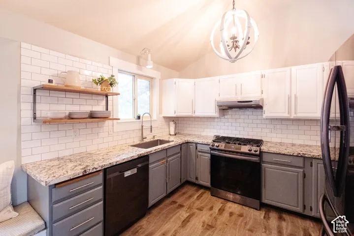 Vaulted ceiling with an orb chandelier, L-shaped kitchen featuring wood-finish flooring, two-tone cabinetry, subway tile backsplash, and stainless steel appliances