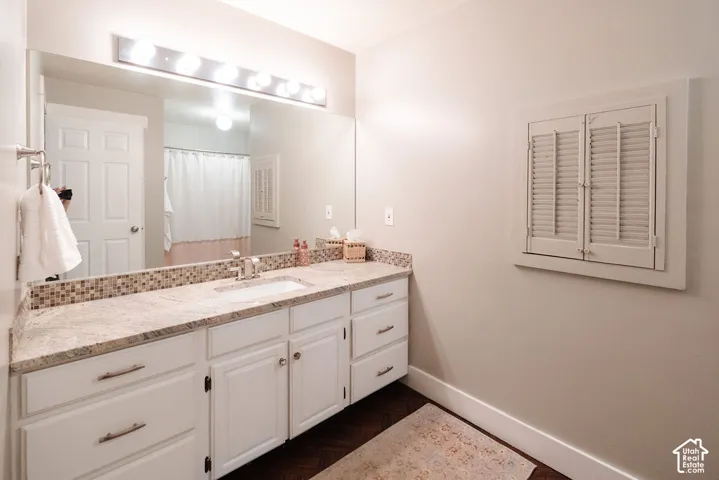 Dual sink vanity with stone countertop, mosaic tile backsplash, and white cabinetry