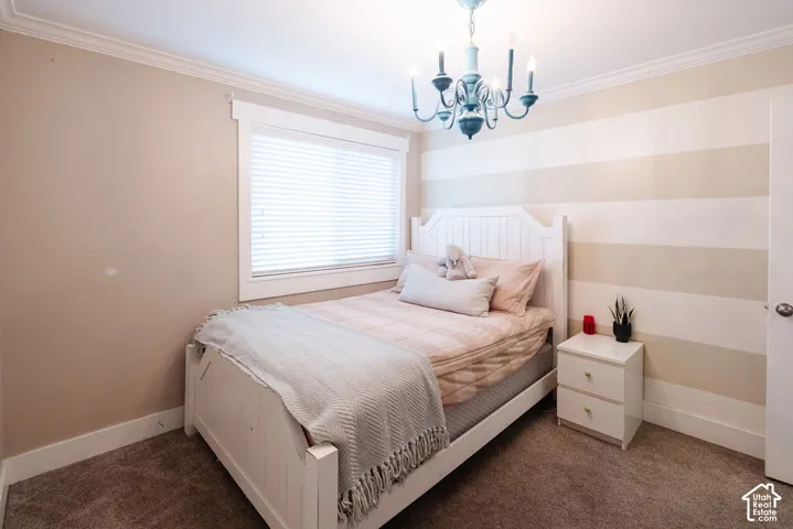Crown molding, window with blinds, striped accent wall, ceiling-mounted chandelier, and carpeted flooring