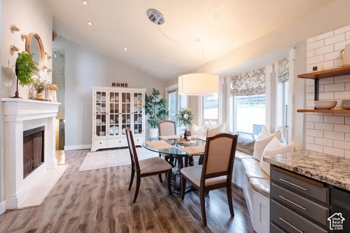 Vaulted ceiling, wood-finish flooring, white fireplace with hearth, built-in window seating, and subway tile backsplash