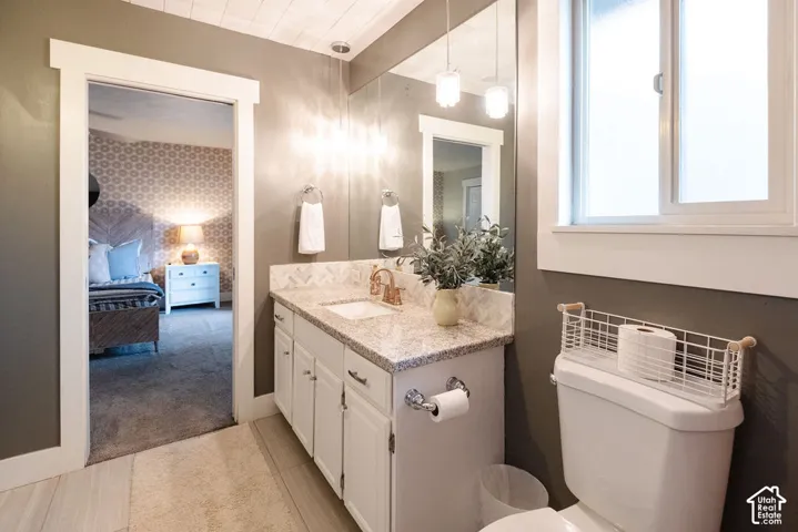 Bathroom featuring a granite countertop, white vanity cabinetry, wall-mounted mirror, and a window