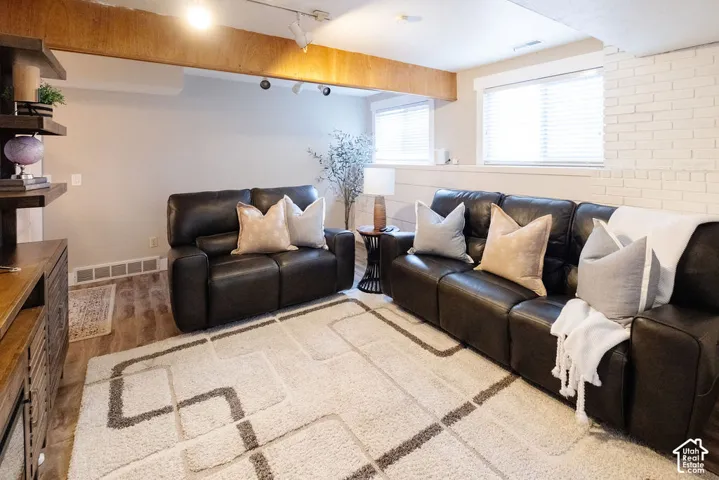 Exposed wood beam, wood-finish flooring, recessed lighting, and white-painted brick wall