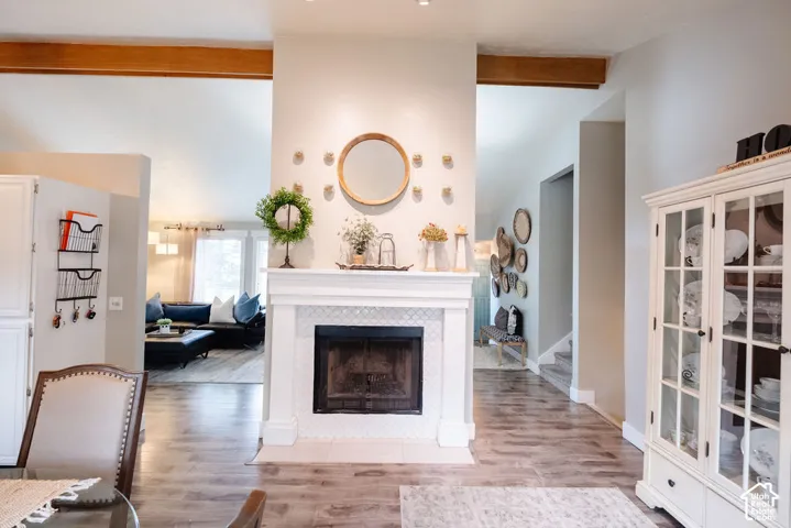 Fireplace featuring a white mantel and tile surround, exposed wood beams, and wood-finish flooring