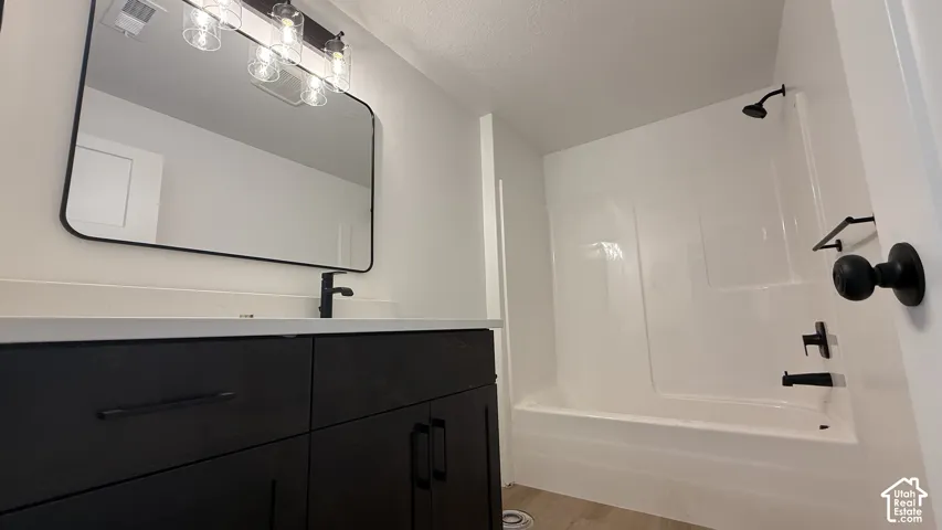 Bathroom featuring a dark wood-finish vanity with a light-colored countertop, a black-framed rectangular mirror, and a white tub with a shower