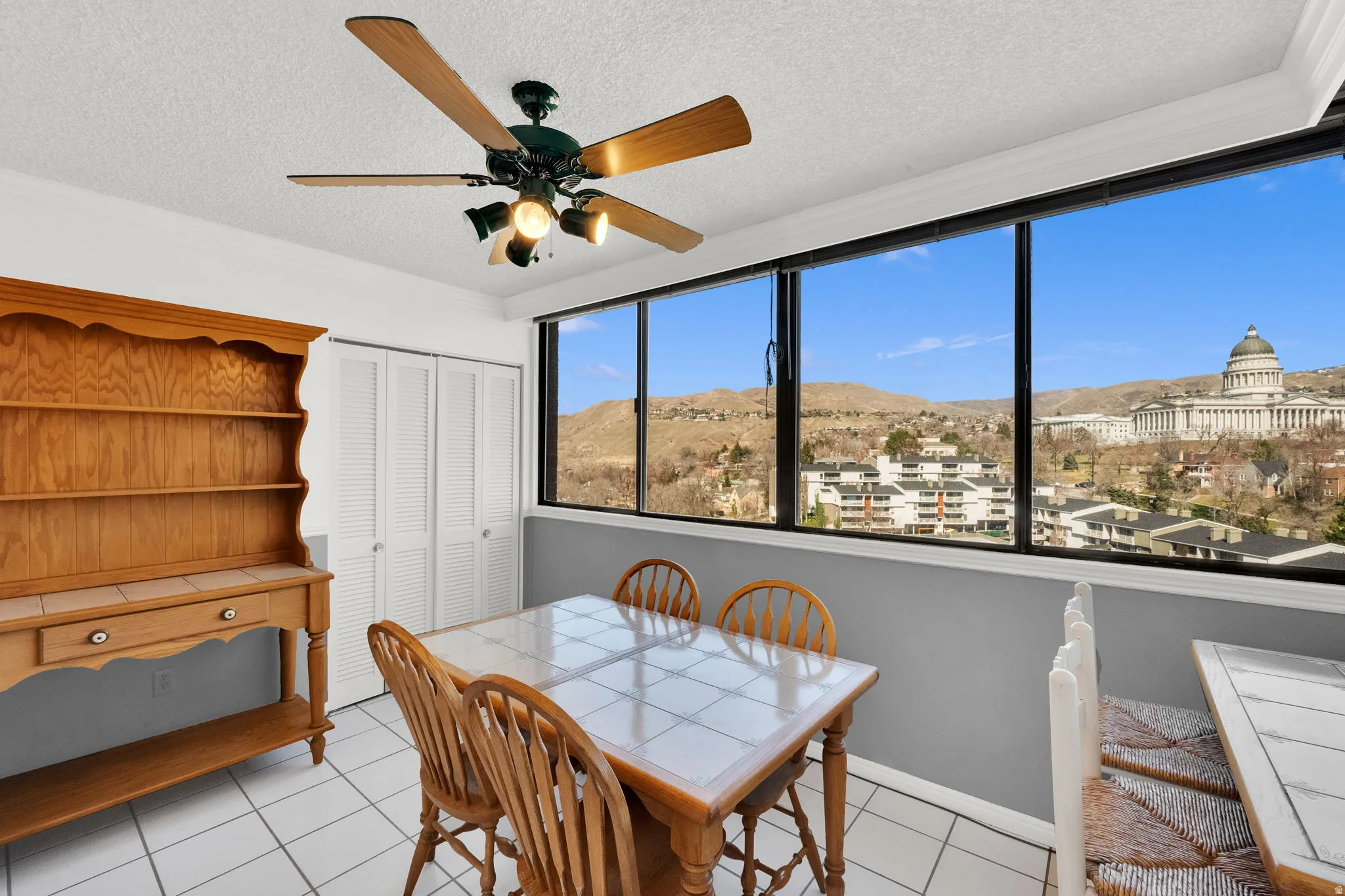 White tile flooring, full-length windows, ceiling fan with integrated lighting, bi-fold closet doors, and distant architectural landmark
