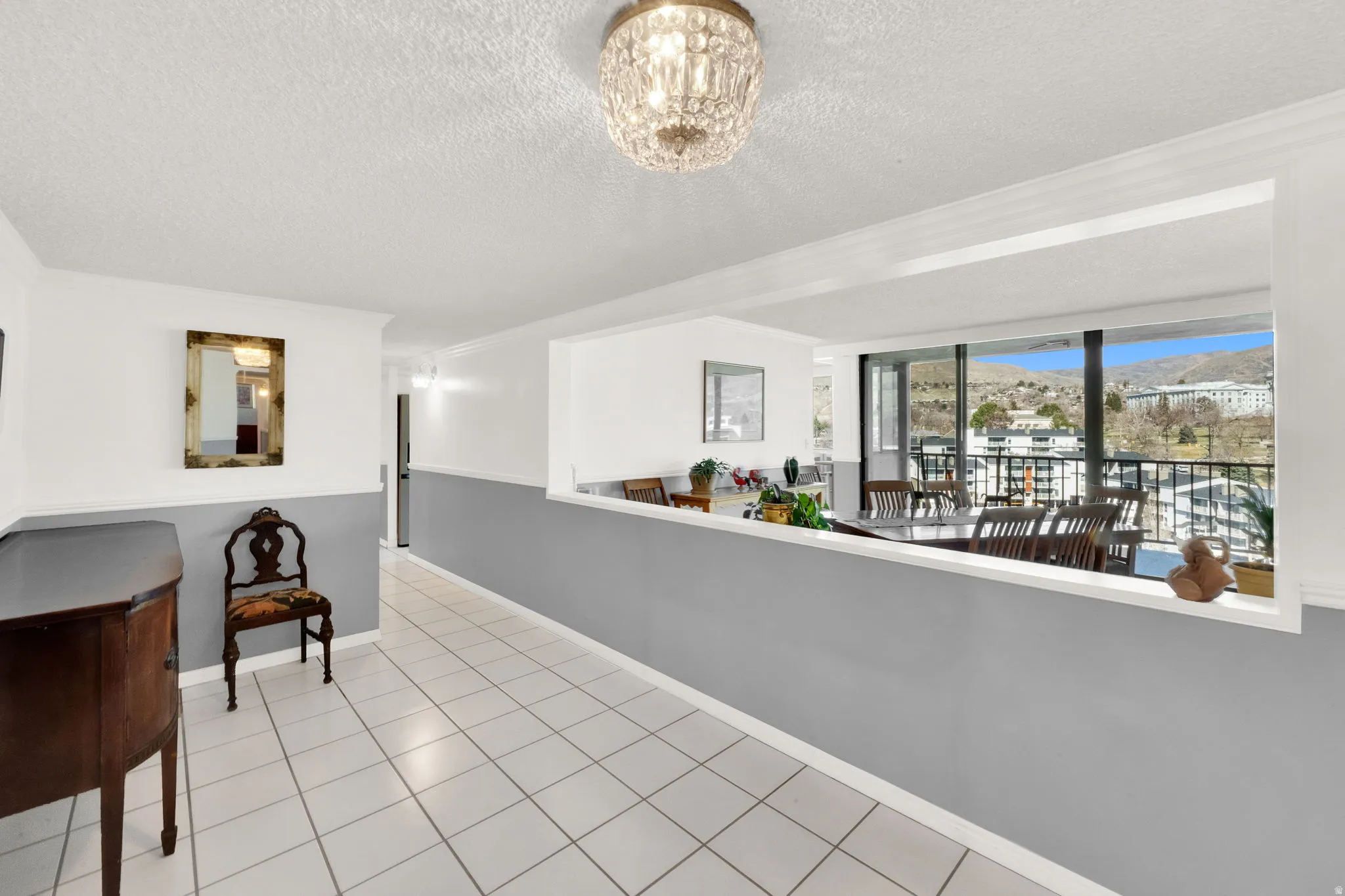 White tile flooring, half-wall room divider, crystal flush-mount lighting, expansive window panels, and balcony access
